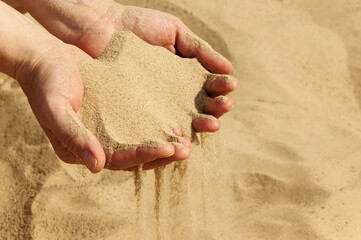 Handful of sand in the women's hands, selective focus. The sand pouring from female hands.