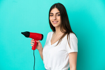 Young caucasian woman holding a hairdryer isolated on blue background smiling a lot