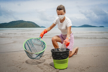 A female ecologist volunteer cleans the beach on the seashore from plastic and other waste