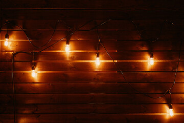 Vintage hanging incandescent lamps on wires. Wooden wall with light bulbs. Loft party interior. Rustic background with copy space. Scene decoration for country festival.