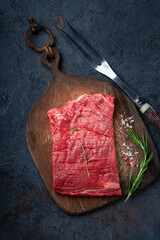 Raw flank steak or Flat iron steak on a wooden board with grilling seasonings, top view