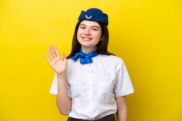 Airplane stewardess Russian woman isolated on yellow background saluting with hand with happy expression