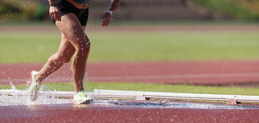 Runner running through the steeplechase water bake on a running track, steeplechase females...