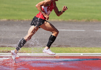 Runner running through the steeplechase water bake on a running track, steeplechase males athletes runner overcame water jump