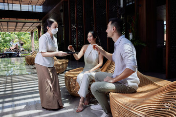 Receptionist greeting asian couple guest with welcome drink at lobby after arrival who are waiting...