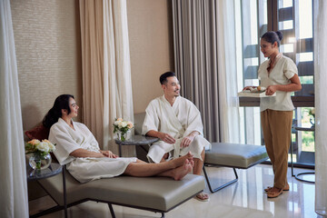 Young asian couple in white bathrobes spending a weekend or celebrating honeymoon at spa and enjoying wellness tea. Resort and beauty salon concept