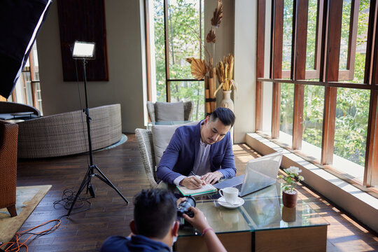 Professional male photographer takings pictures of businessman writing notes. Behind the scene in photography industry. Filming stock photography content - Powered by Adobe