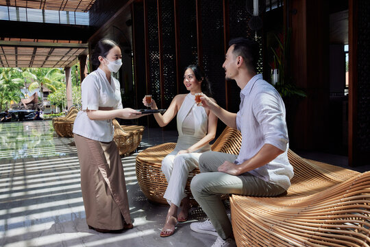 Receptionist greeting asian couple guest with welcome drink at lobby after arrival who are waiting for hotel check in