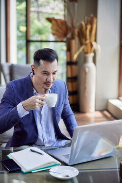 Young handsome asian businessman having a video call using a laptop, sitting in cafe or coworking space. Conference call or working online