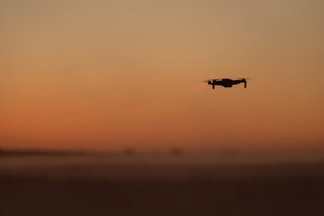 Fototapeta na wymiar A quadcopter is flying in the fog in the orange sunset sky