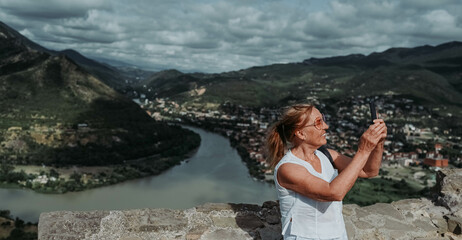Mature woman tourist takes pictures on observation deck confluence of two rivers Aragvi and Kura,...
