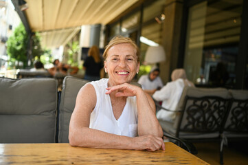Happy senior woman with perfect smile and teeth sitting outdoors at summer sidewalk street cafe or restaurant terrace. Retired mature people holiday vacation, active lifestyle concept