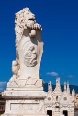 Fototapeta na wymiar Marble lion statue, erected in 1875 in Pisa historical center, with beatiful St. Mary of the Thorn gothic church in the background