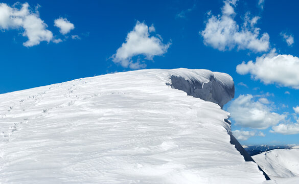 Winter mountain top with fairy overhang snow cap and human footprint on snowy mountainside follow up.