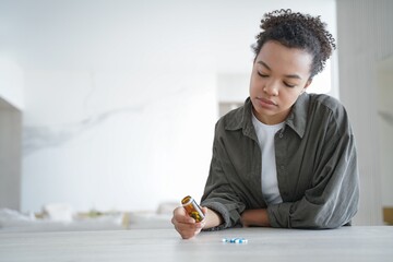 Pensive young woman holds bottle with medicines doubt whether to take pills. Healthcare. Copy space