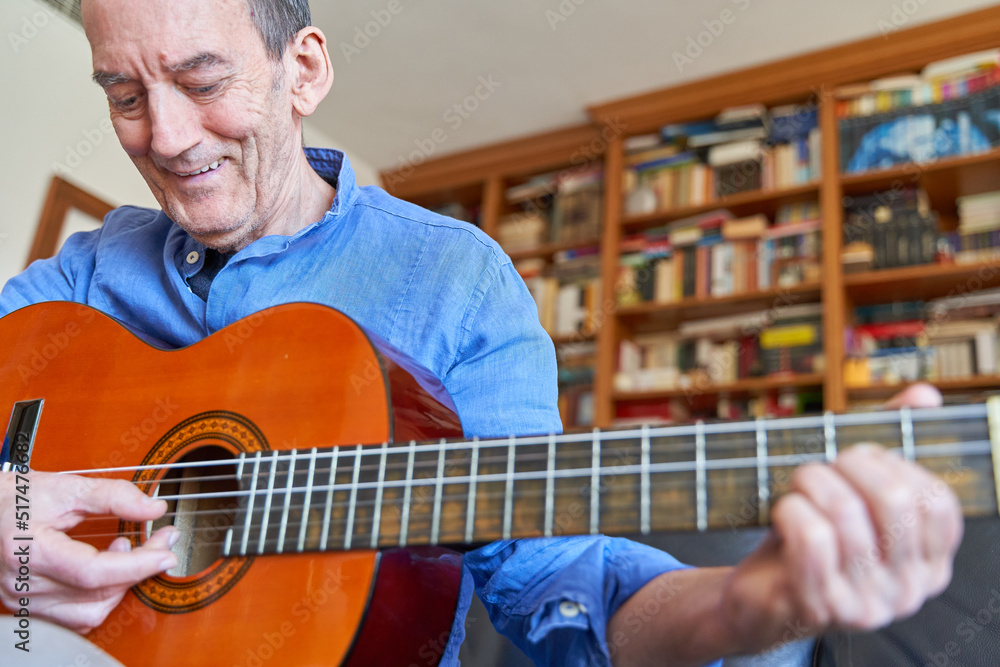 Wall mural smiling elderly man playing classical guitar with library on background