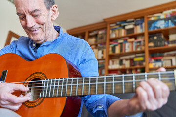 Smiling elderly man playing classical guitar with library on background