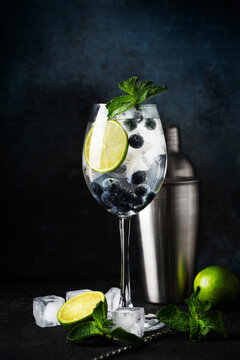 Alcohol cocktail with lime, blueberry, ice cube and mint on dark background,