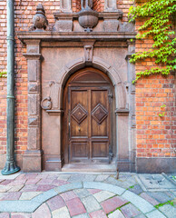 Ornamental wooden arched door framed by engraved marbles in a red brick wall and colorful...