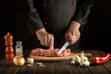 Butcher or chef cuts raw veal meat on a cutting board before barbecue. Cooking delicious food in the hotel kitchen