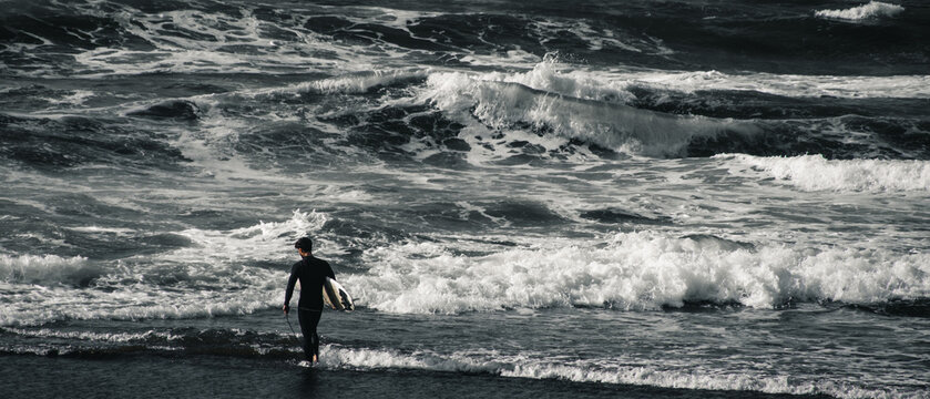 surfer in a wetsuit enters a beach with waves to surf