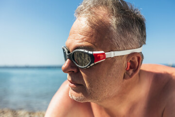 Mature man with glasses diving and silicone ear plugs on beach.