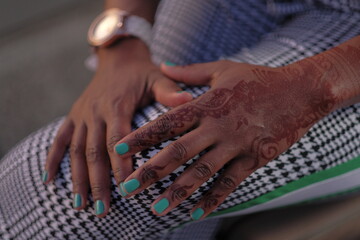 Black woman's hand with Arabic henna tattoo rests on crossed legs wearing black and white...
