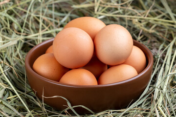 Gray chicken eggs in a clay bowl on a background of hay.