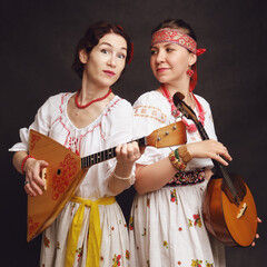 Women musicians in Russian folk dresses with musical instruments on a black studio background....