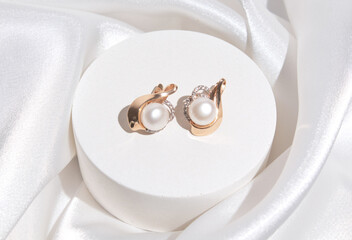 Pearl earrings with golden fittings on white silk background. Beautiful accessories for women....