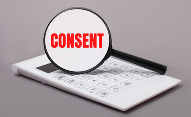On a gray background, a white calculator and a magnifying glass with the text CONSENT. Business concept