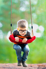 Blond boy with glasses on a swing in the park. The joy