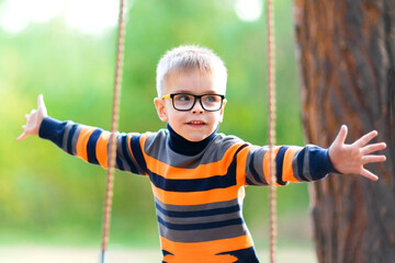 Blond boy with glasses on a swing in the park. The joy