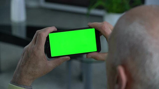 Senior person holds smartphone with empty green screen in hands and watching social nets