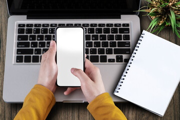 Male hands working on smartphone and modern laptop. Office desktop on wooden table background. Top view with copy space, flat lay.
