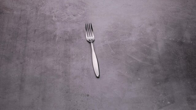 A glossy fork is spinning on the table, cutlery video on a gray background.
