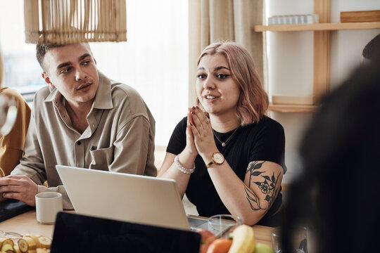 Female entrepreneur with hands clasped discussing while sitting by male colleague during meeting in office