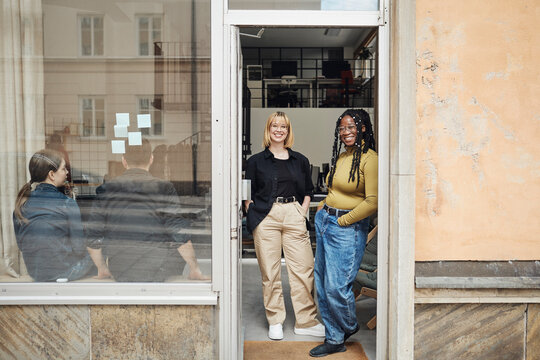 Female computer programmers standing at doorway of tech start-up office