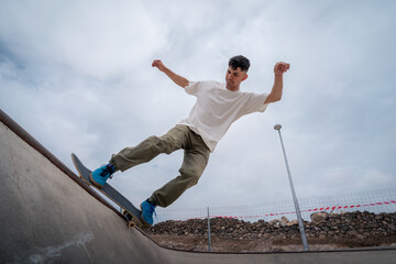 young male skater skates over the edge of a bowl at a skate park - obrazy, fototapety, plakaty