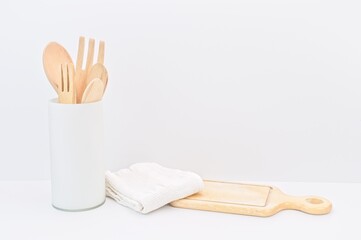 utensili da cucina in legno in contenitore di vetro con tagliere e canovaccio in cotone su tavolo e sfondo bianco