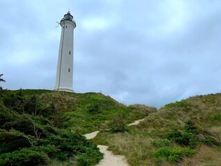 Fototapeta na wymiar white lighthouse Lyngvig Fyr in a beautiful dune landscape with a sandy trail at a cloudy day, Hvide Sande, Søndervig, Ringkøbing, Denmark
