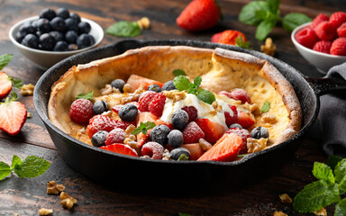 Dutch baby pancake with berries and icing sugar in a iron cast pan. Morning breakfast