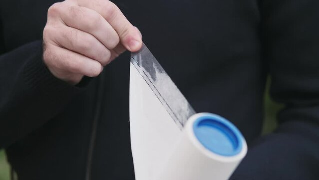 Close-up of a man's hand with a clothes roller, lint roller or sticky roller removing animal hair and fluff from clothes
