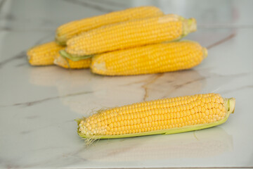 many gold ear of corns vegetable on a white marble background