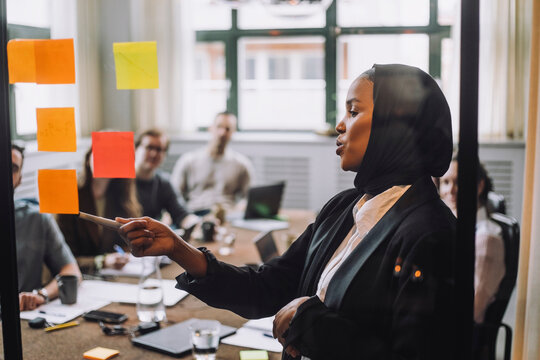 Young businessman wearing headscarf explaining adhesive notes to colleagues during meeting in creative office