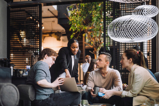 Young businesswoman discussing over laptop with male and female colleagues while sharing ideas in office