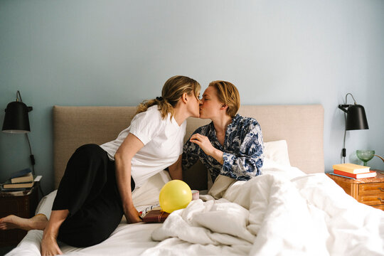 Lesbian woman with birthday present kissing girlfriend on bed at home