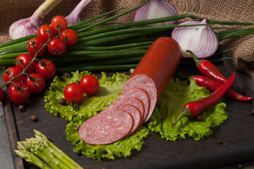 smoked servelat on a wooden board decorated with fresh vegetables