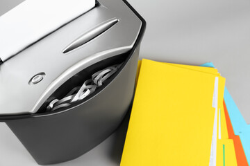 Shredder with sheet of paper and colorful folders on grey background, above view. Space for text