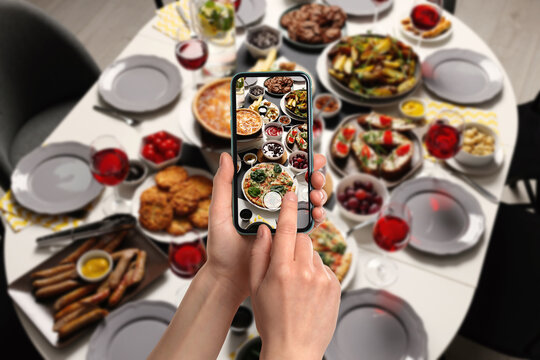 Woman taking picture of table with different delicious food indoors, above view